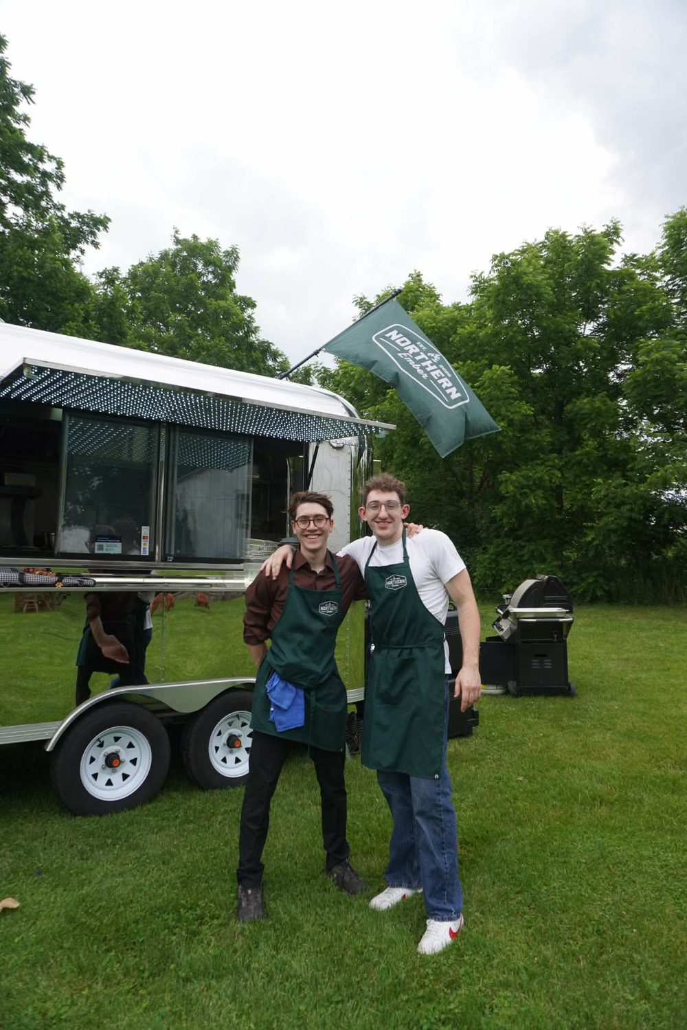 Two Northern Ember staff in green aprons in front of the food truck at a wedding